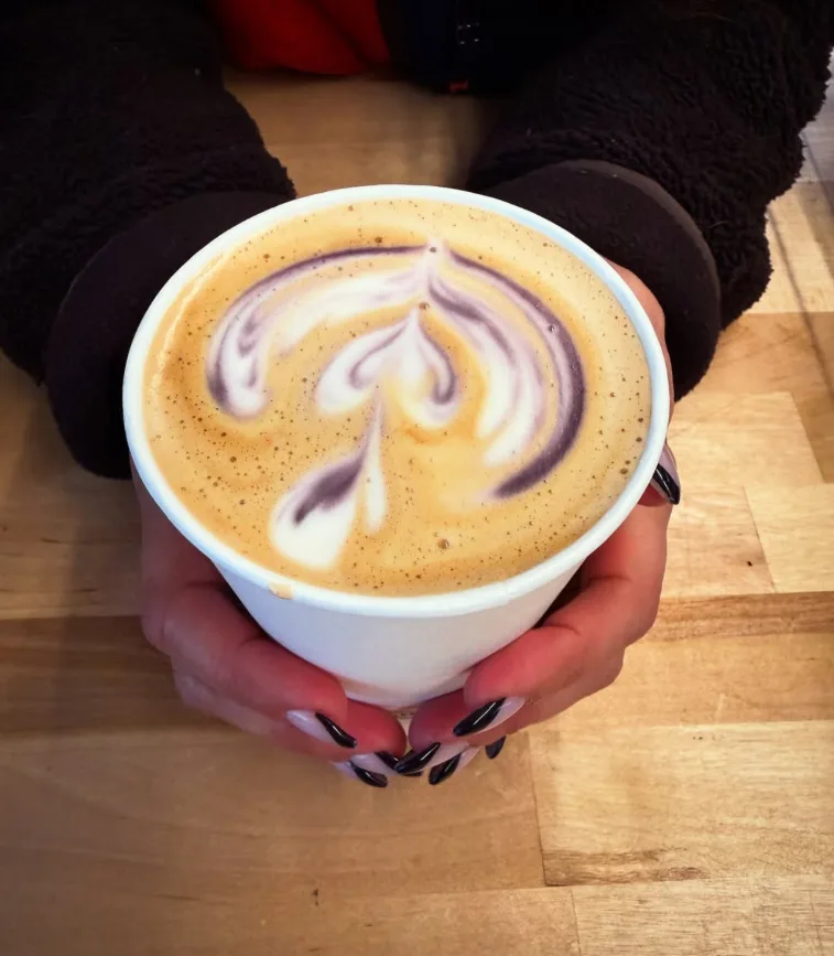 A latte with purple swirls in the foam, held in two hands