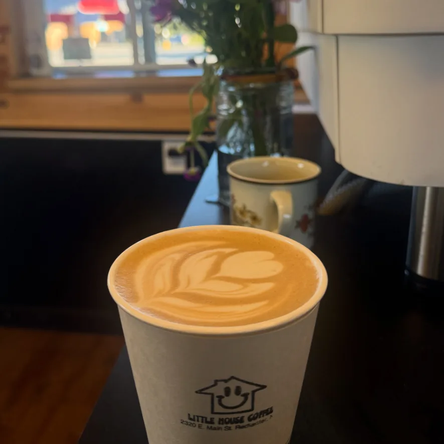 A latte with a leaf in the foam, in a Little House Coffee cup on the counter