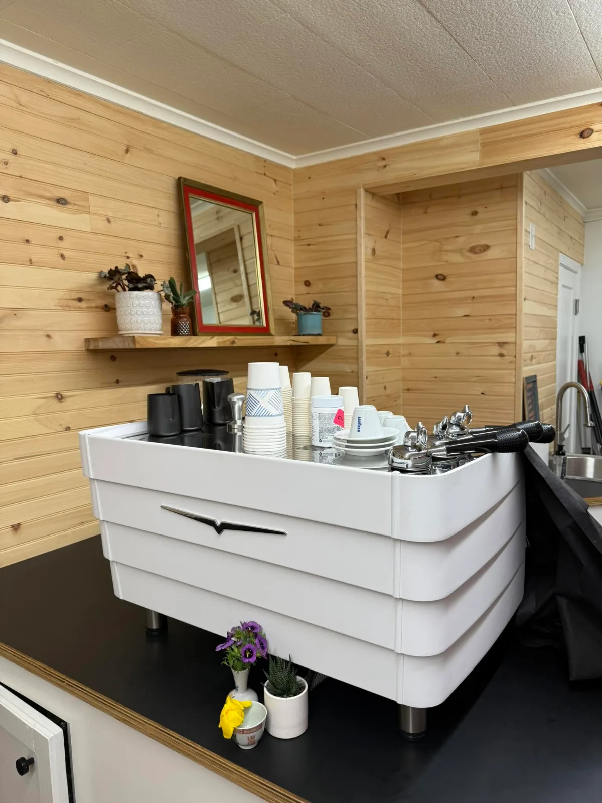 The espresso machine on the counter against pine-paneled walls, with cups stacked on top